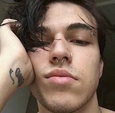 a man with piercings on his nose is looking at the camera while holding his hand to his ear