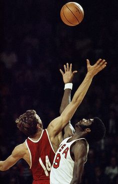 two men playing basketball in front of an audience at a sporting event, one reaching for the ball