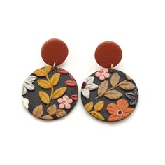 a pair of earrings with flowers and leaves painted on the back of them, sitting on top of a white surface