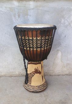 an african drum on display in front of a concrete wall with a giraffe design