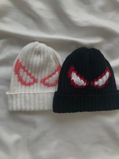 two knitted hats with red eyes on them sitting next to each other in front of a white sheet