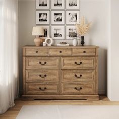 a wooden dresser sitting next to a window with pictures on the wall above it and a lamp