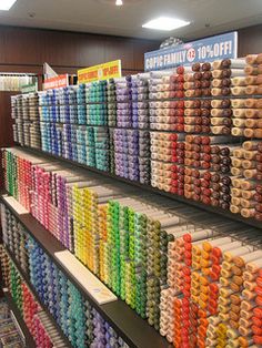 rows of different colored spools of thread on display in a store with lights