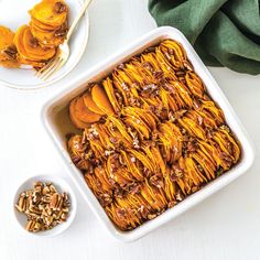 a casserole dish filled with sweet potatoes and pecans next to a bowl of nuts