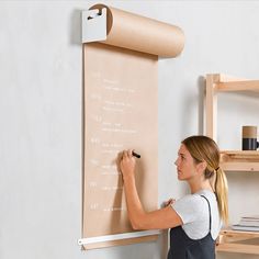 a woman writing on a bulletin board with a pen and paper roll in front of her