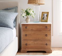 a wooden dresser sitting next to a bed with blue sheets and pillows on top of it