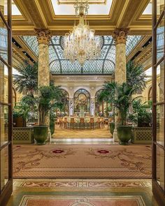 an open door leading to a dining room with chandelier and potted plants