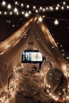 a bed covered in white sheets and lights under a canopy with a tv on it