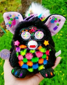 a hand holding a small stuffed animal with multicolored decorations on it's face