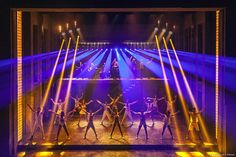 a group of people on stage with their arms in the air and lights shining down