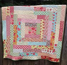 a pink and green quilt hanging on a wooden fence