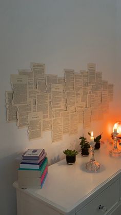 a white dresser topped with lots of books next to a wall covered in papers and candles