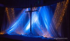 a cross on top of a stage covered in blue fabric with lights and curtains behind it