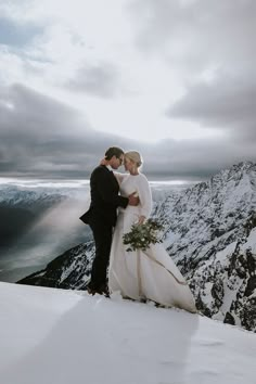 a bride and groom standing on top of a snow covered mountain