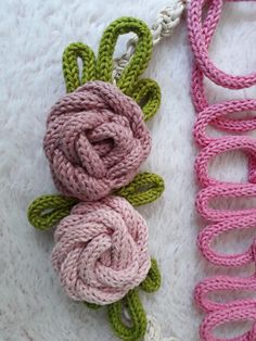 two crocheted flowers are laying next to each other on a white surface with pink and green yarn