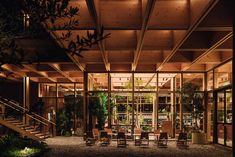 the inside of a building lit up at night with chairs and plants on the ground