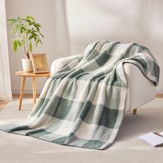 a green and white blanket sitting on top of a couch next to a potted plant