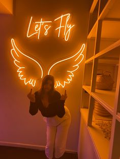 a woman standing in front of a neon sign that says let's fly on it