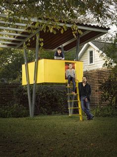 two men are standing on a ladder in front of a yellow structure that is attached to a house