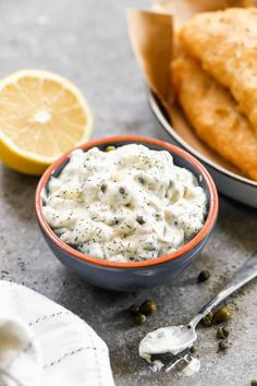 a bowl filled with white sauce next to some bread and lemon wedges on the side