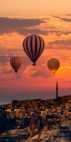 three hot air balloons flying over a city at sunset