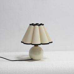 a white table lamp sitting on top of a white bed next to a black cord