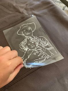 a person is drawing on a piece of paper with white ink while holding onto a pair of black pants