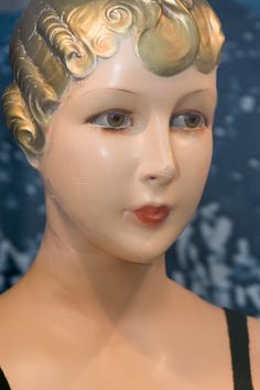 a mannequin's head with gold hair and curls on it, in front of a blue background