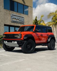 a bright orange truck parked in front of a building with palm trees and blue sky