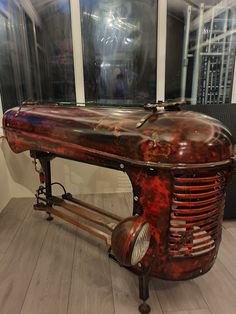 an old red and black machine sitting on top of a hard wood floor next to windows