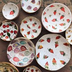 many plates with strawberries painted on them sitting on the ground next to each other