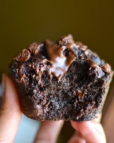 a person holding a chocolate donut with frosting on it