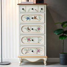 a white dresser with flowers painted on it and a potted plant next to it