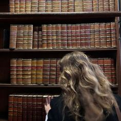 a woman standing in front of a bookshelf filled with lots of old books