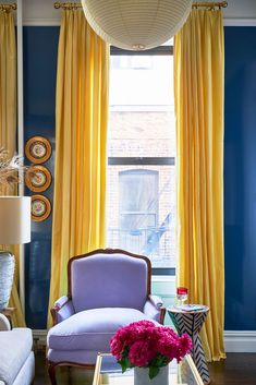 a living room with blue walls and yellow drapes on the windowsill, purple chair, and coffee table