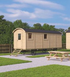 two wooden cabins sitting on top of a grass covered field next to a picnic table