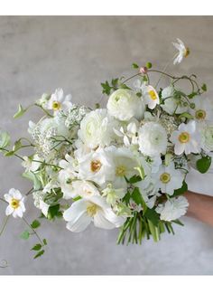 a bouquet of white flowers is held by a person's hand in front of a gray wall