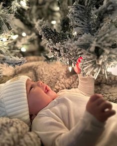 a baby laying on top of a blanket next to christmas trees