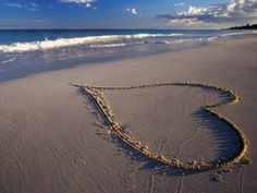 a heart drawn in the sand on a beach with an ocean and sky behind it