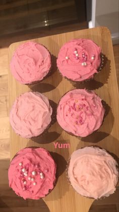 cupcakes with pink frosting and sprinkles on a wooden board