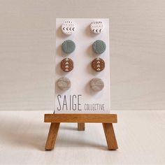 three pairs of earrings sitting on top of a wooden stand in front of a white wall