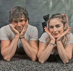 a man and woman laying on the ground next to each other with their hands under their chins