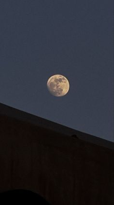 the moon is shining brightly in the night sky above a building with an arched roof