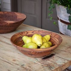 a wooden bowl filled with pears sitting on top of a table next to another bowl