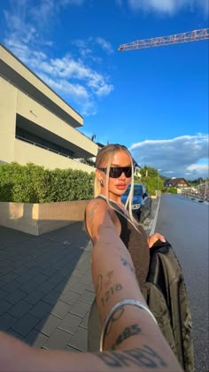 a woman with tattoos on her arm pointing at the camera while standing in front of a building