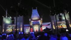 the entrance to star wars is lit up at night with palm trees and people standing around