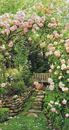 a garden filled with lots of pink flowers next to a stone wall and wooden bench