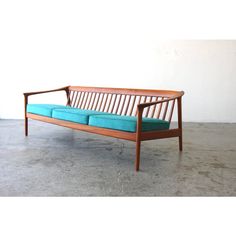 a wooden bench sitting on top of a cement floor next to a white wall and blue cushions