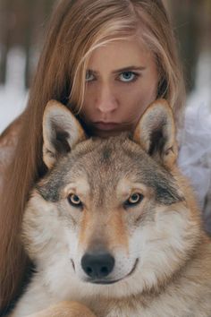 a woman with long hair and blue eyes is holding a wolf in her arms while looking at the camera