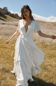 a woman in a white dress is walking through the grass